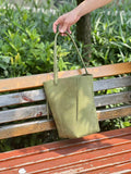 Minimalist green leather bucket bag with shoulder strap on a wooden bench outdoors