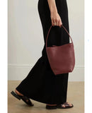 Minimalist large tan leather bucket bag with single handle, held by woman in black dress