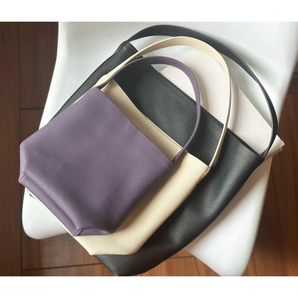 Three minimalist leather tote bags in purple, cream, and black on a white chair