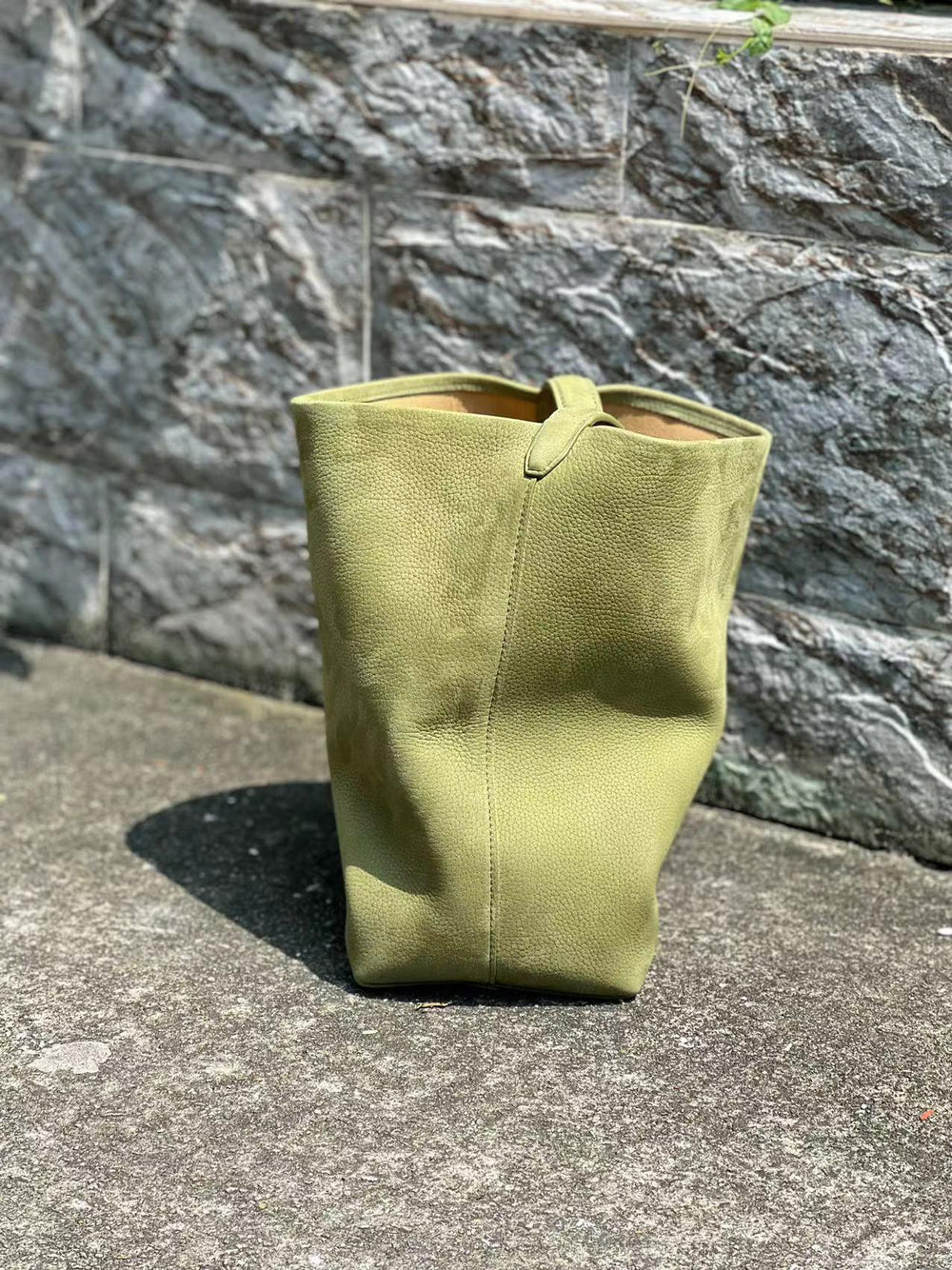 Minimalist tan leather bucket bag with textured surface on outdoor stone pavement