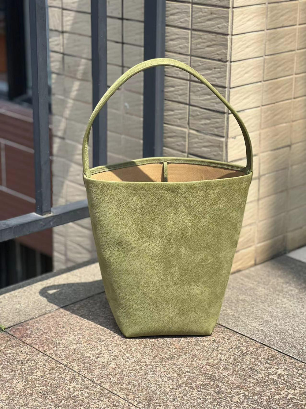 Minimalist olive green leather bucket bag with single handle, large tote on outdoor stone step