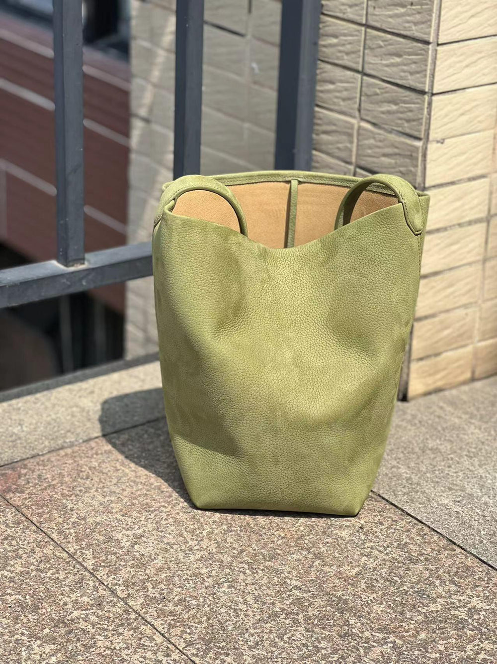 Minimalist green leather bucket bag with handles, large unisex tote on outdoor stone surface