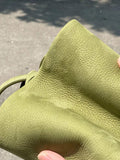 Close-up of textured green leather bucket bag in sunlight, minimalist and unisex style