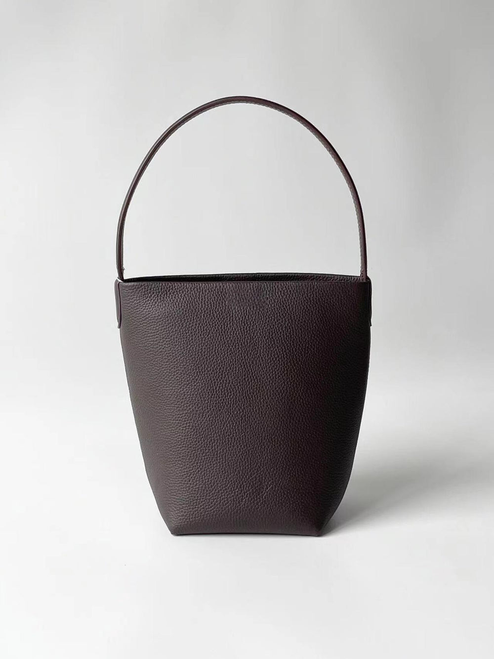 Minimalist brown leather bucket bag with single handle on plain white background