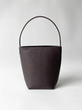 Minimalist brown leather bucket bag with single handle on plain white background