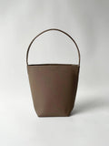 Minimalist tan leather bucket bag with single shoulder strap on plain background