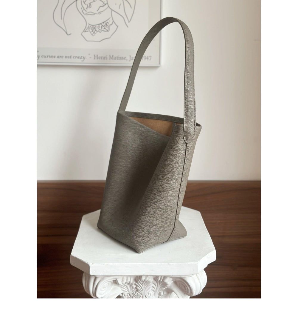 Minimalist taupe leather bucket bag with wide strap on display against neutral background
