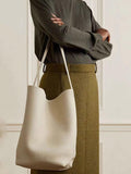 Minimalist tan leather bucket bag with shoulder strap, worn by person in neutral outfit.