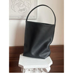 Minimalist black leather bucket bag with single strap on white pedestal, modern background