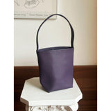 Minimalist purple leather bucket bag with shoulder strap on a white pedestal