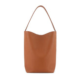 Minimalist tan leather bucket bag with single shoulder strap on white background