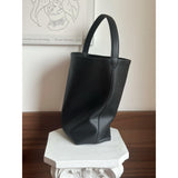 Minimalist black leather bucket bag with single shoulder strap on a white pedestal indoors