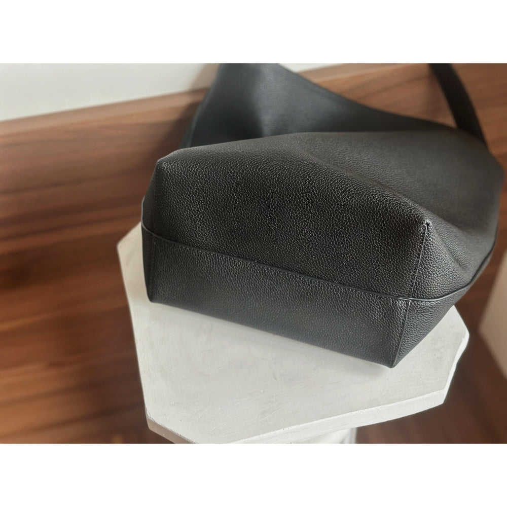 Minimalist black leather bucket bag with textured finish on white table