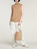 Woman holding minimalist tan leather bucket bag, styled with white pants and beige top