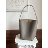 Minimalist large tan leather bucket bag with single shoulder strap on white pedestal indoors