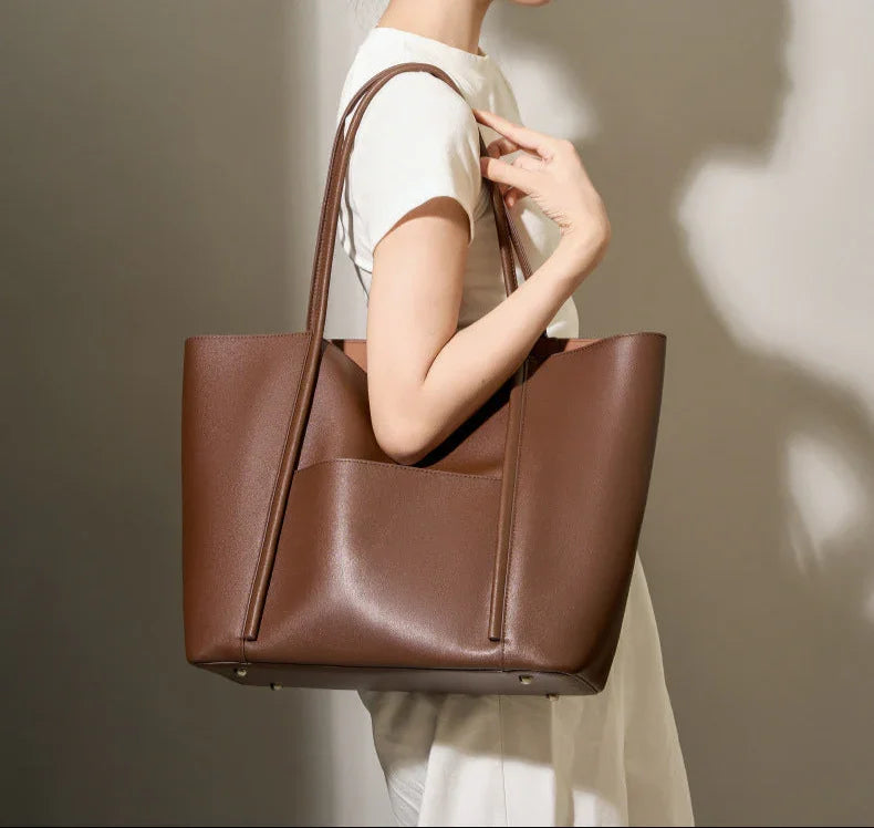 Woman carrying large brown minimalist genuine leather tote handbag with top handles