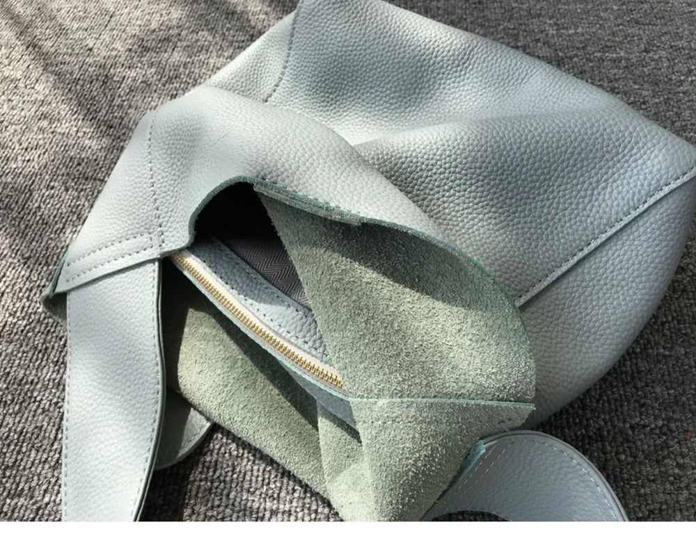 Minimalist pebbled cowhide leather bucket bag with wide shoulder strap on textured surface