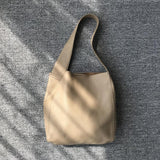 Minimalist beige pebbled cowhide leather bucket bag with wide shoulder strap on grey background