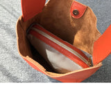 Inside view of an orange pebbled leather bucket bag with a wide strap and inner zip pouch