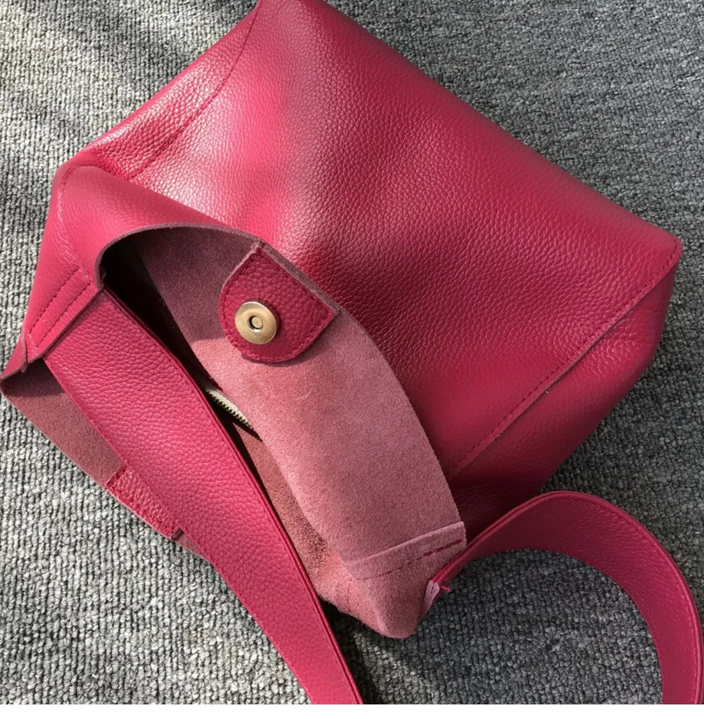 Minimalist pebbled red cowhide leather bucket bag with wide shoulder strap on gray fabric