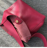 Minimalist pebbled red cowhide leather bucket bag with wide shoulder strap on gray fabric
