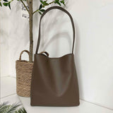 Minimalist brown pebbled cowhide leather bucket bag with wide shoulder strap on white background