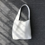 Minimalist white pebbled cowhide leather bucket bag with wide shoulder strap on gray fabric