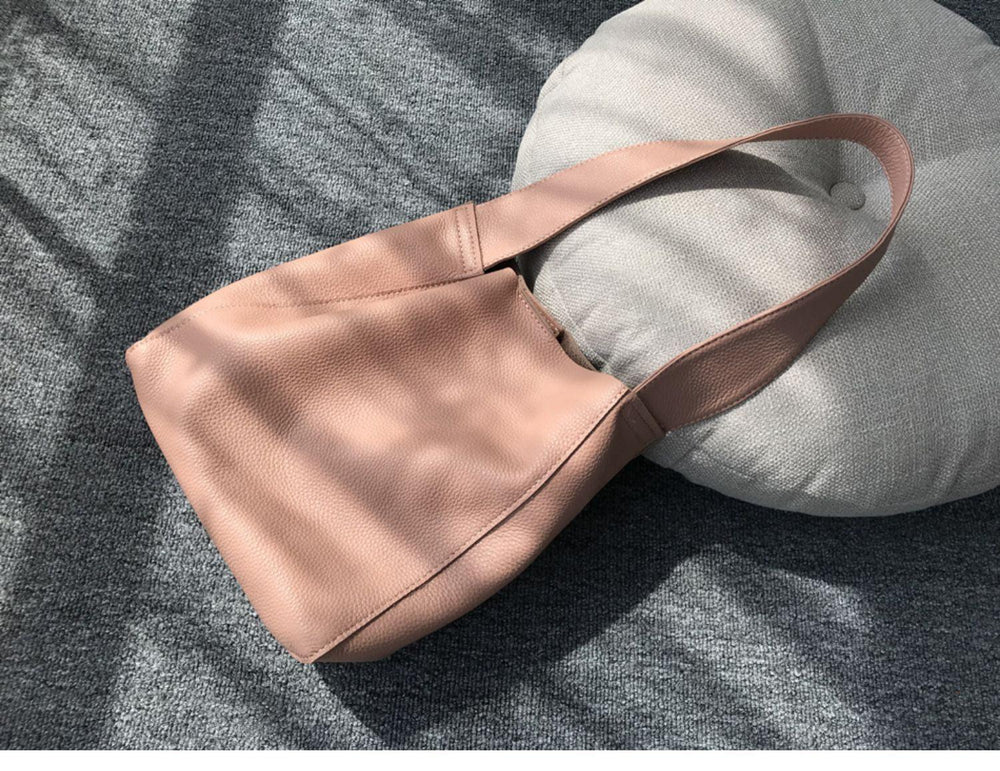 Minimalist pebbled cowhide leather bucket bag with wide shoulder strap on grey carpet