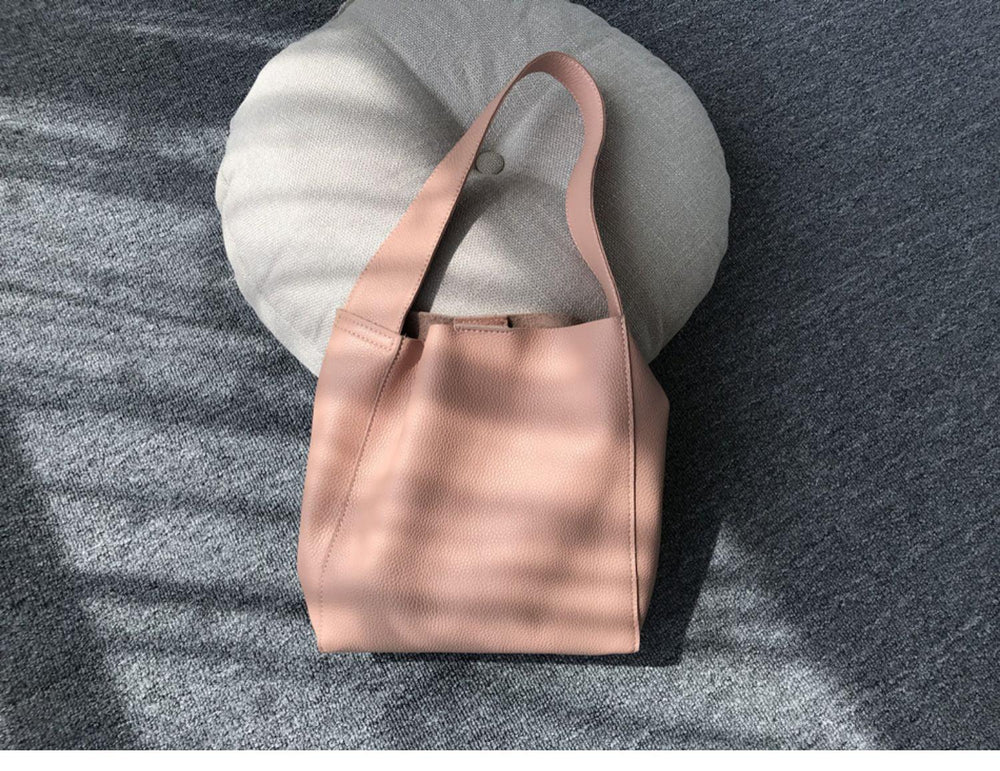 Minimalist pebbled cowhide leather bucket bag with wide shoulder strap on grey fabric