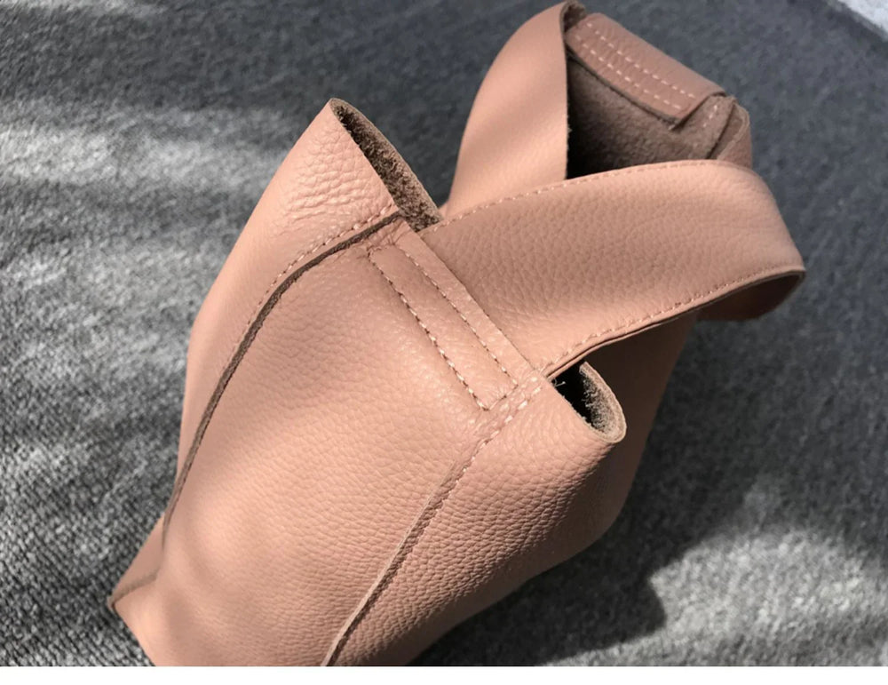 Minimalist pebbled cowhide leather bucket bag with wide strap on grey surface