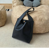 Minimalist black pebbled cowhide leather bucket bag with wide shoulder strap on beige pouf