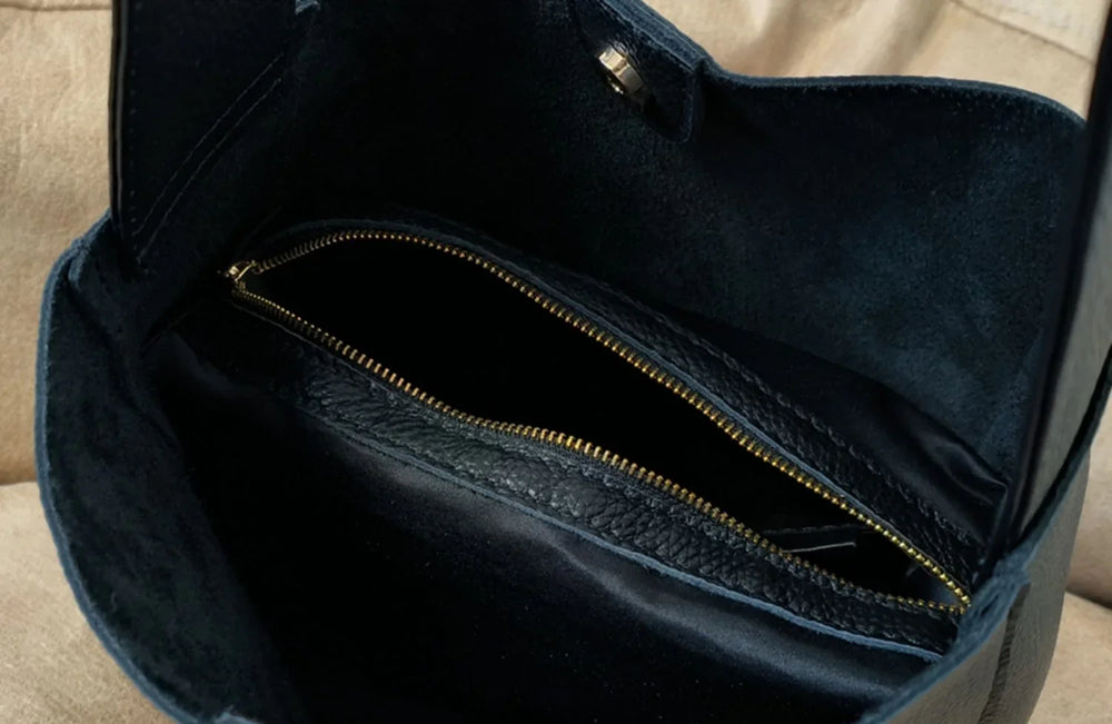 Interior of a black pebbled leather bucket bag with gold zipper pocket and suede lining