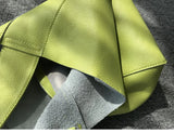 Minimalist green pebbled cowhide leather bucket bag with wide shoulder strap on fabric surface
