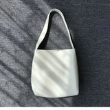 Minimalist white pebbled cowhide leather bucket bag with wide shoulder strap on grey fabric