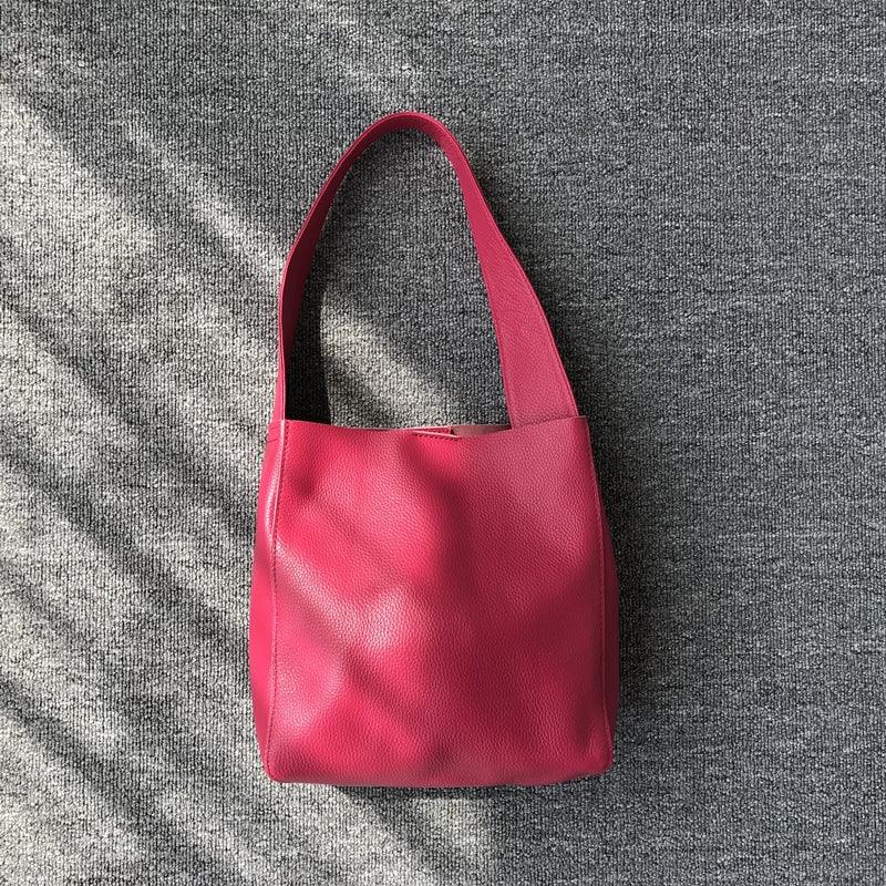 Minimalist pink pebbled cowhide leather bucket bag with wide shoulder strap on grey fabric