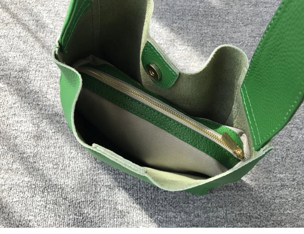 Green pebbled leather bucket bag with wide shoulder strap, interior zipper pouch, on grey fabric.