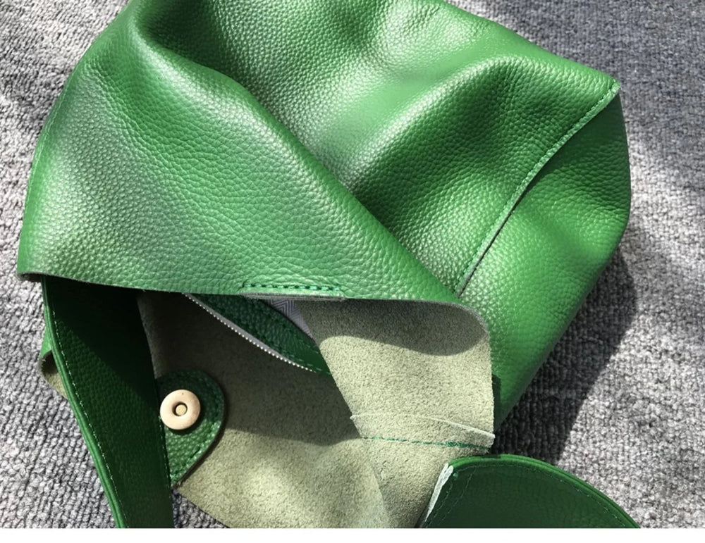 Green pebbled cowhide leather bucket bag with wide shoulder strap on gray textured surface