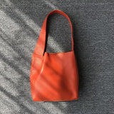 Minimalist orange pebbled cowhide leather bucket bag with wide shoulder strap on gray fabric