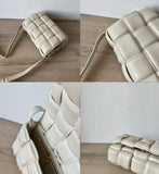 Cream woven leather crossbody bag with shoulder strap and gold zipper, on wooden surface