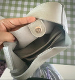 Hand opening a light gray leather purse with magnetic snap and zippered inner pocket