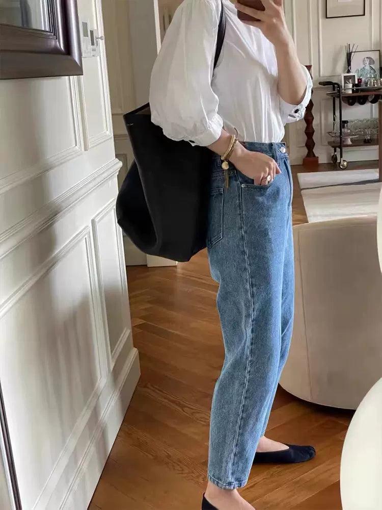 Woman wearing a white blouse, blue jeans, black flats, and carrying a large black leather tote bag