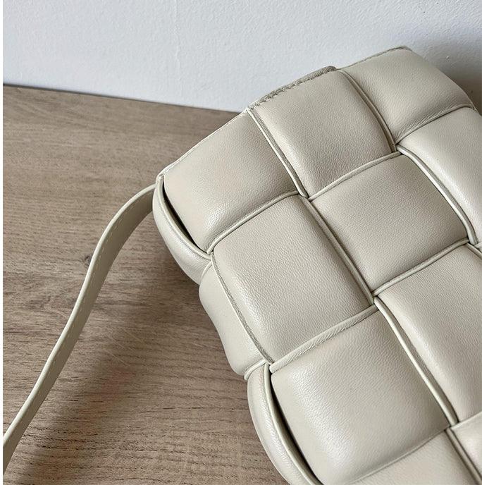 Close-up of a beige woven leather crossbody bag on a wooden surface