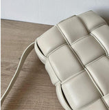 Close-up of a beige woven leather crossbody bag on a wooden surface