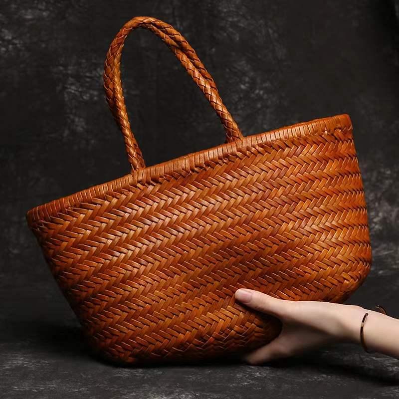 Hand holding a large woven leather tote bag with braided handles on a dark background