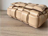 Beige woven leather handbag with padded texture on wooden surface