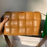 Hand holding a tan woven leather crossbody bag with padded square pattern