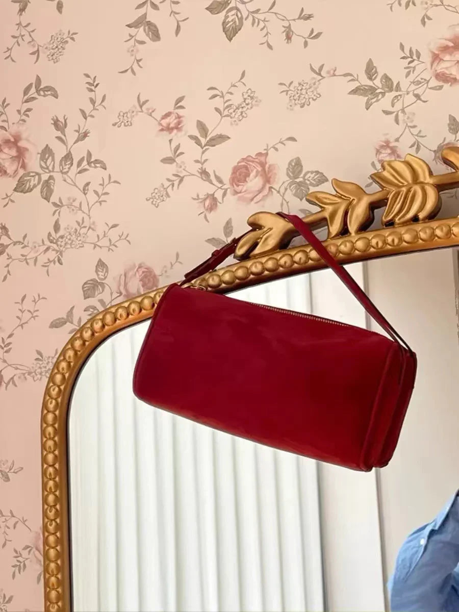 Red suede leather handbag with strap on ornate gold mirror, floral wallpaper background