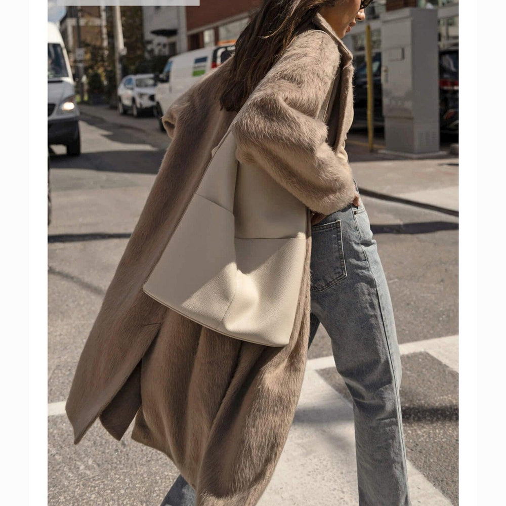 Woman wearing a large beige leather tote bag with front pockets, walking outdoors in casual outfit.