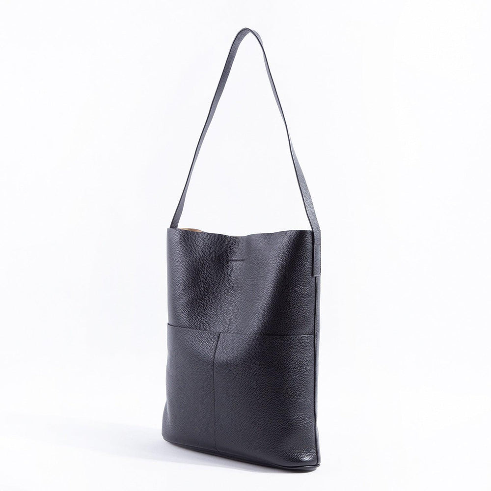 Black cowhide leather tote bag with two front pockets and a single shoulder strap, minimalist design.
