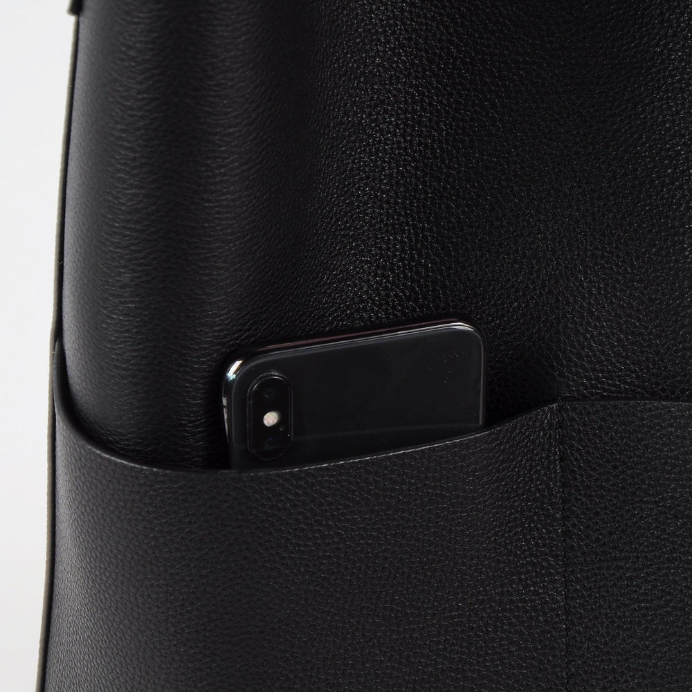 Black cowhide leather tote bag with front pocket holding a smartphone, minimalist design